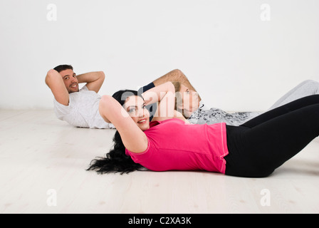 Aktive glückliche Familie, die auf hölzernen Boden tun Sit Ups für flache abs, paar auf die Kamera und lächelnd Stockfoto