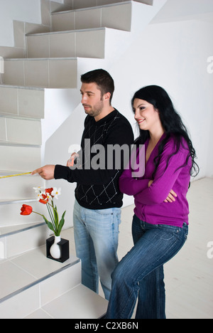 Junges Paar Umzug in neues Haus, sie messen die Treppe und Planung zusammen in einem leeren Raum mit weißen Holzboden Stockfoto