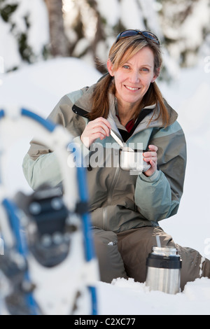 Kaukasische Frau mit Schneeschuhen im Schnee Essen Stockfoto