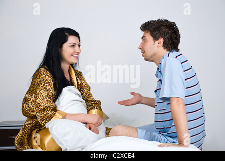 Junges Paar mit einem Gespräch in ihrem Bett, der Mann etwas zu erklären ihr und Gestikulieren mit seiner Hand Stockfoto