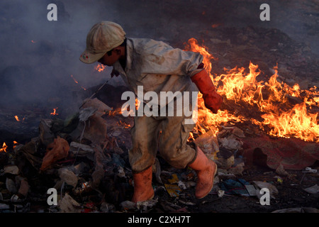 Ein junges Kind Arbeiter junge läuft weg von einem Haufen brennenden Müll in einer verschmutzten Müllkippe in Kambodscha. Stockfoto