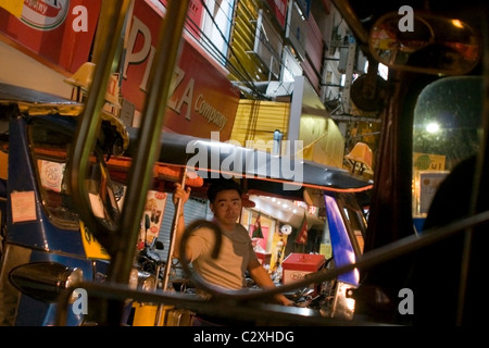 Eine männliche Tuk-Tuk-Fahrer wartet auf Kunden in der Nacht auf einer hellen Stadtstraße in Chiang Rai, Thailand. Stockfoto