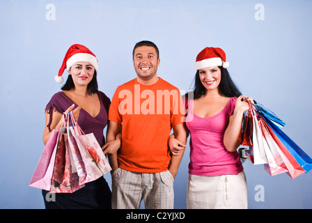 Glücklich drei Freunde halten Weihnachten Einkaufstaschen und Lächeln für Sie auf blauem Hintergrund Stockfoto