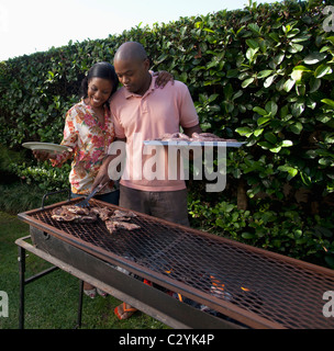 Frau umarmt Mann Kochen von Fleisch auf dem Braai, Johannesburg, Südafrika Stockfoto