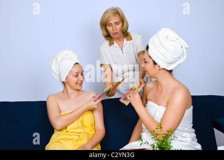 Ein senior Arbeitnehmerin in einem Spa resort gebende Zeitschriften, zwei Frauen, die auf der Couch sitzen und warten auf Behandlungen Stockfoto