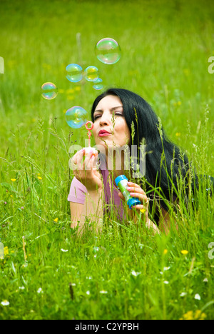 Schöne Brünette Frau grüne Frühling Gras auf einer Wiese liegen und Seifenblasen Stockfoto