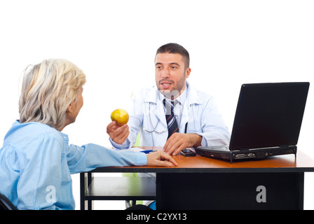 Arzt männlich senior Frau Patient in seinem Büro einen Apfel anzubieten Stockfoto