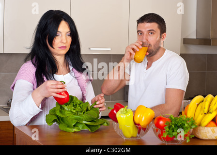 Mitte erwachsenes paar in Küche man trinkt Orangensaft und die Frau bereitet das Abendessen Stockfoto