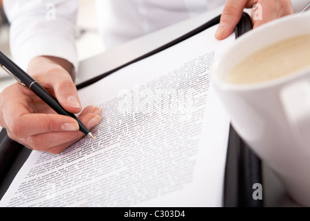 Nahaufnahme der Geschäftsfrau von Hand mit Stift über Dokument mit weißen Tasse in der Nähe von Stockfoto