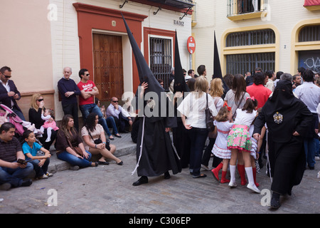 Mit Kapuze Büßer (Nazarenos) versammeln sich zum Sevillas jährliche Semana Santa Leidenschaft Osterprozessionen. Stockfoto