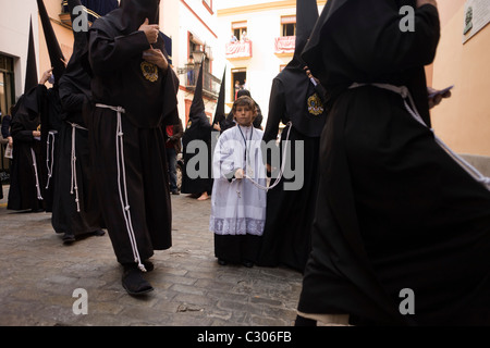 Chorknabe und vermummte Büßer (Nazarenos) versammeln sich zum Sevillas jährliche Semana Santa Leidenschaft Osterprozessionen. Stockfoto