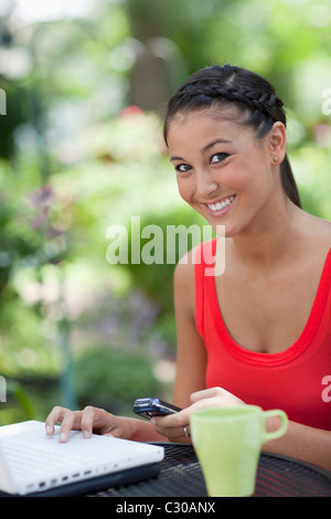 Schöne asiatische Frau verwendet einen Laptop und Handy. Sie lächelt in die Kamera im Freien. Vertikale erschossen. Stockfoto