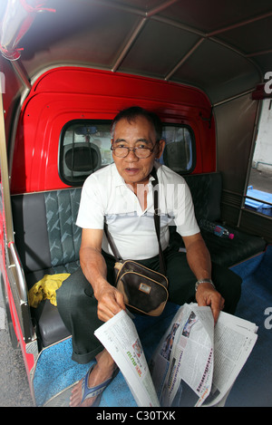 Tuktuk Fahrer liest seine Zeitung in der Rückseite seines Fahrzeugs. Stockfoto