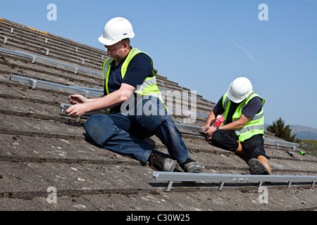 Zwei Männer passend Schienen für solar pv panel Anhaftung an Hausdach Wales UK Stockfoto