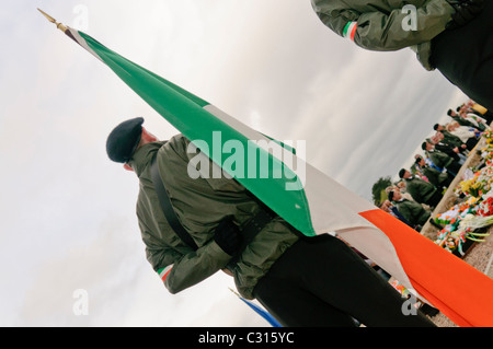 Männer, gekleidet in paramilitärischen Uniformen, und Vertreter der Sinn Féin, der politische Flügel der Irisch-Republikanischen Armee (IRA), halten Sie die Irische trikolore Flaggen während der jährlichen Ostern steigende Gedenken, Belfast, Nordirland. Stockfoto