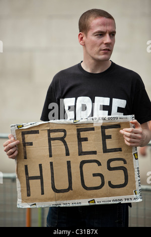 Porträt eines jungen Mannes, der ein Schild „Free Hugs“ an einem öffentlichen Ort hält, London, England, Großbritannien Stockfoto