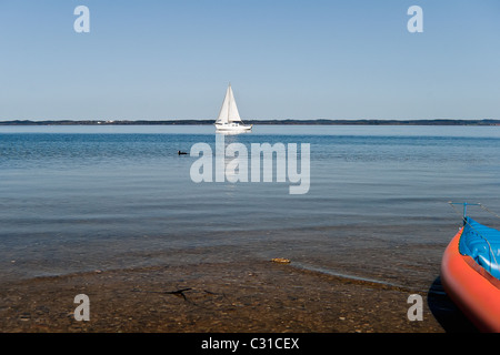 Blick auf den See mit Segelboot und farbigen Kanu in einem ruhigen, sonnigen Tag Stockfoto