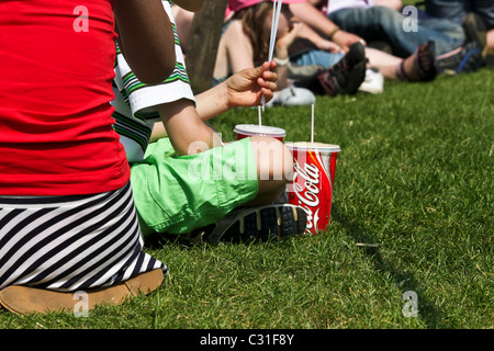 Kinder (nicht identifizierbar) sitzen auf dem Rasen und trinken Coca cola Stockfoto