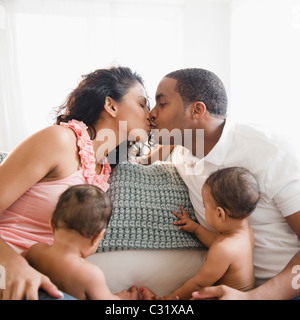 Eltern auf Sofa neben Twin Baby Boys küssen Stockfoto