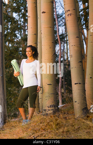 Gemischte Rassen Frau mit Yoga-Matte im Wald Stockfoto