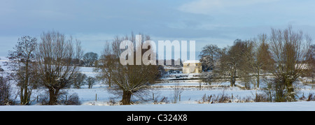 Georgian Manor House und verschneite Felder durch den River Windrush in Dorf Swinbrook, Cotswolds, Großbritannien Stockfoto