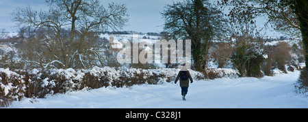 Einsamer Wanderer entlang verschneite Fahrspur im Windrush Tal Swinbrook, The Cotswolds Stockfoto