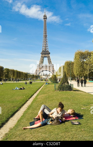 Blick auf den Eiffelturm aus dem Parc du Champ de Mars in Paris. Junge Menschen entspannen auf dem Rasen Stockfoto