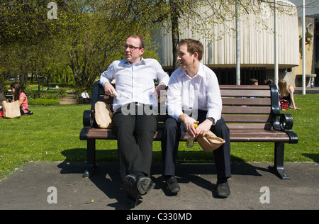 Zwei Kollegen mit Mittagessen auf einer Parkbank an einem Sommertag Stockfoto