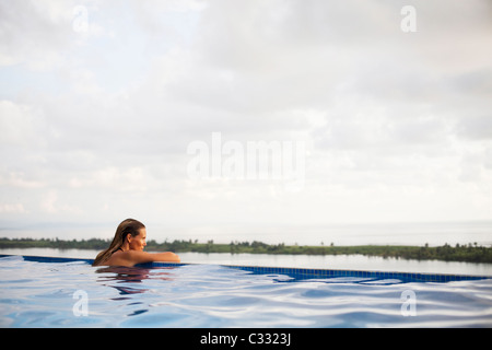 Eine Frau sitzt mit ihren Armen auf den Rand des einen Infinity-Pool mit Blick auf den weiten Ozean. Stockfoto