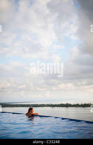 Eine Frau sitzt mit ihren Armen auf den Rand des einen Infinity-Pool mit Blick auf den weiten Ozean. Stockfoto