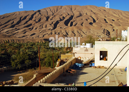 Oman, Wadi Bani Khalid, Häuser vom Fächerpalme Bäume und Strommasten mit Bergen im Hintergrund in der Wüste Stockfoto