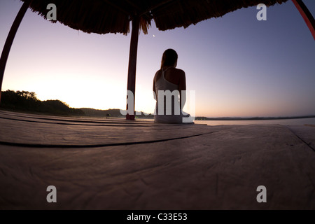 Eine schöne junge Frau schaut die Sonne unterging und der Mond am Ende einen Steg steigen, die über See Petén Guatemalas aussieht. Stockfoto