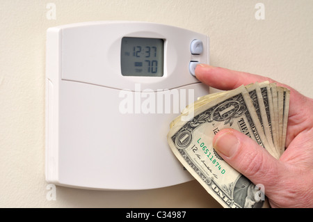 Eine Hand umklammerte US-Dollarnoten, da es nach unten dreht sich der Temperatur am Thermostat für Wärme für Einsparungen. USA Stockfoto