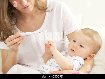 Schreiendes Baby, die ihre Körpertemperatur mit digital-Thermometer von der Mutter genommen Stockfoto