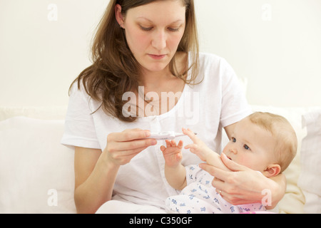 Schreiendes Baby, die ihre Körpertemperatur mit digital-Thermometer von der Mutter genommen Stockfoto