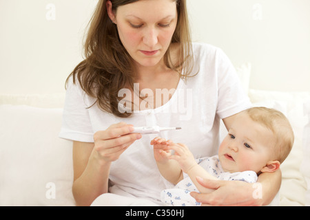 Schreiendes Baby, die ihre Körpertemperatur mit digital-Thermometer von der Mutter genommen Stockfoto