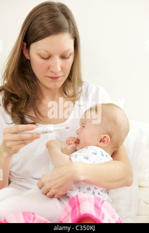 Schreiendes Baby, die ihre Körpertemperatur mit digital-Thermometer von der Mutter genommen Stockfoto