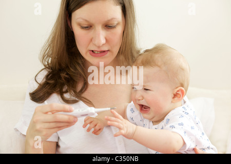 Schreiendes Baby, die ihre Körpertemperatur mit digital-Thermometer von der Mutter genommen Stockfoto