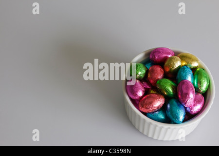 Eine Schüssel mit winzigen Schokoladeneier, eingehüllt in Multi-farbigen Folie vor einem grauen Hintergrund. Stockfoto