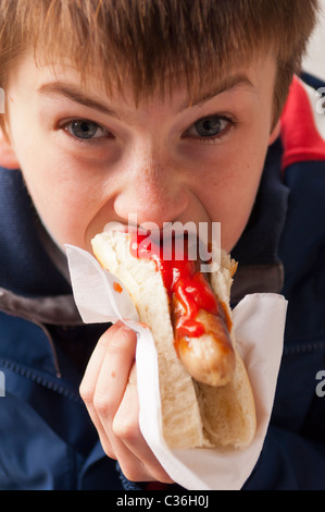 Ein elfjähriger Junge Essen einen Hot Dog mit Tomaten-Ketchup-Sauce im Vereinigten Königreich Stockfoto