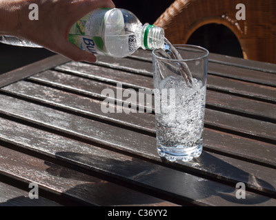 Gießen ein Glas Mineralwasser aus einer Plastikflasche auf ein Café im freien Tisch Stockfoto