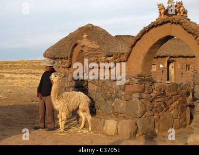 Uro-Bauer mit Lama stand vor seinem Hof. Über dem Eingang ist ein Team von keramischen Büffeln, Puno, Peru. Stockfoto