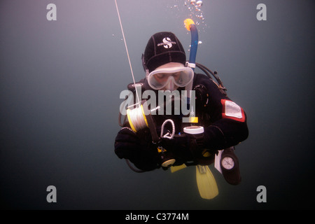 Ein weibliche Taucher überwacht ihren Computer, da sie nach einem Tauchgang einen Sicherheitsstop mit einem bereitgestellten DSMB durchführt. Stockfoto