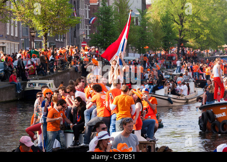 Königstag, der Geburtstag des Königs (Königinnentag Königinnentag) in Amsterdam Mädchen auf Boot winken niederländische Flagge in traditionellen Canal Parade Stockfoto