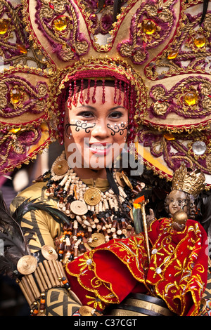 Ein Porträt Filipina Straße Tänzer in vollen braunen Kostüm mit Kopfbedeckung tragen eine geschnitzte Sto. Nino-Figur. Stockfoto