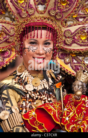 Ein Porträt Filipina Straße Tänzer in vollen braunen Kostüm mit Kopfbedeckung tragen eine geschnitzte Sto. Nino-Figur. Stockfoto