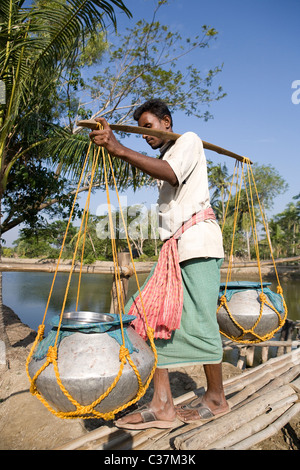 Indischen Mann trägt Töpfe mit Wasser in einem kleinen Dorf in der Sunderbans Nationalpark in West Bengal, Indien. Stockfoto