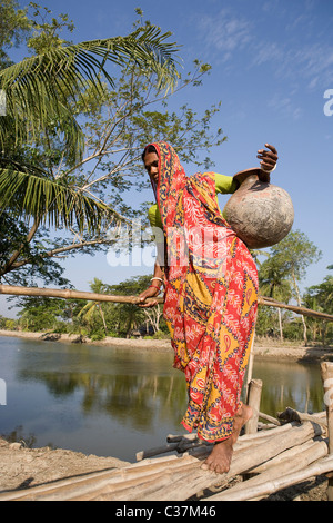Indische Frau trägt einen Topf mit Wasser auf eine kleine Brücke in der Sunderbans Nationalpark in West Bengal, Indien. Stockfoto