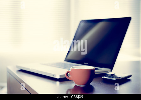 Kaffeepause-Konzept, das Bild zeigen einen Laptop, Handy und eine Tasse Kaffee auf dem Schreibtisch im Hintergrund eine große Fenster Stockfoto