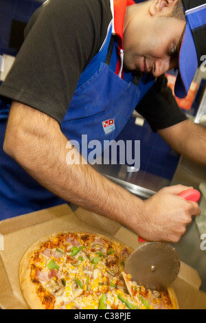 Ein Domino Pizza Mitarbeiter schneidet eine frische Pizza zur Auslieferung bereit. Stockfoto